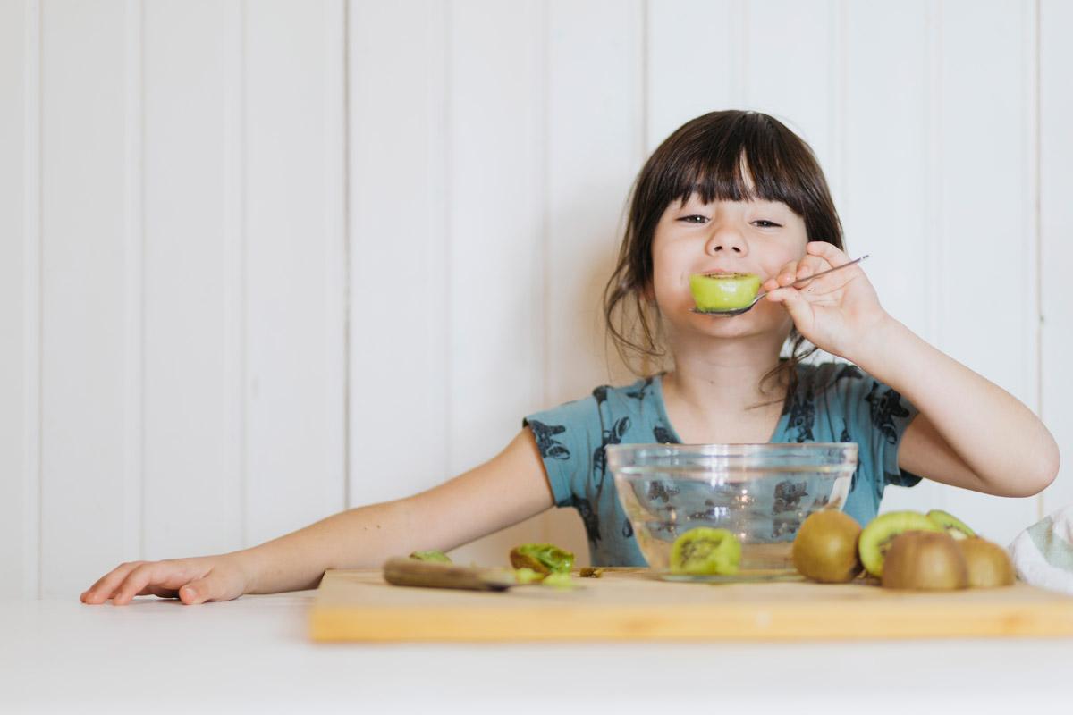 A small girl enjoying a kiwi fruit bowl on dining table