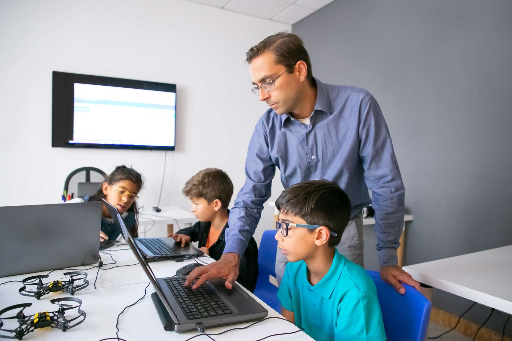 Male teacher teaching children to use computer at computer lab.