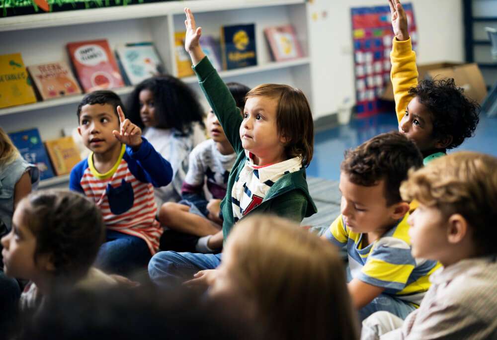 Playschool kids raising hands asking questions.